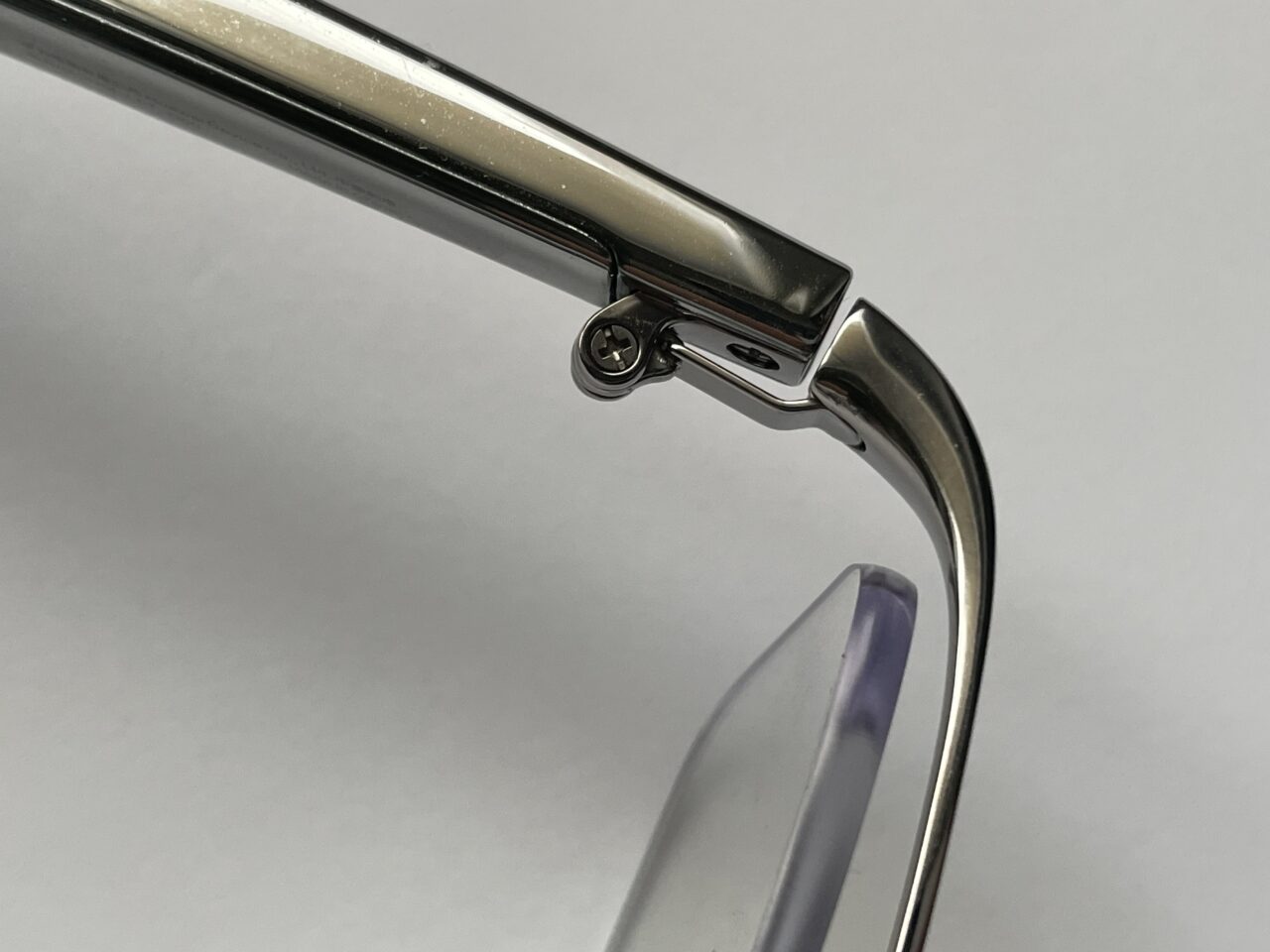 Zbliżenie na metalową ramę okularów z widocznym zawiasem i śrubką na białym tle.