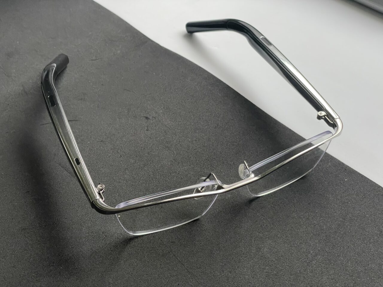 Okulary z przezroczystymi szkłami i metalową oprawką leżące na ciemnoszarym biurku.
