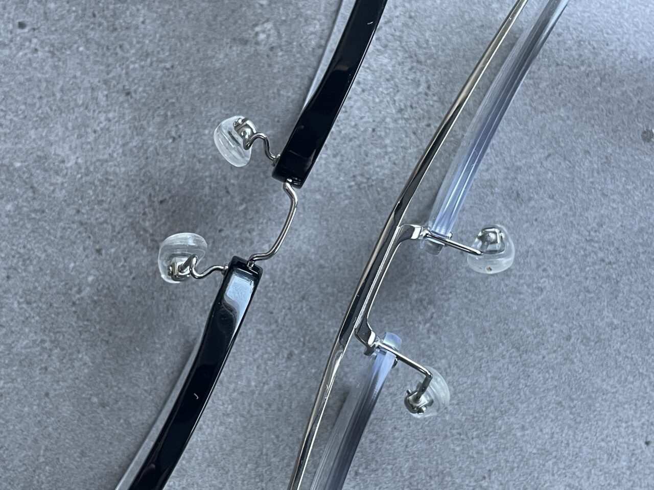 Zbliżenie na noski i zauszniki czarnych okularów z przezroczystymi nakładkami na noski, położonych na szarej powierzchni.