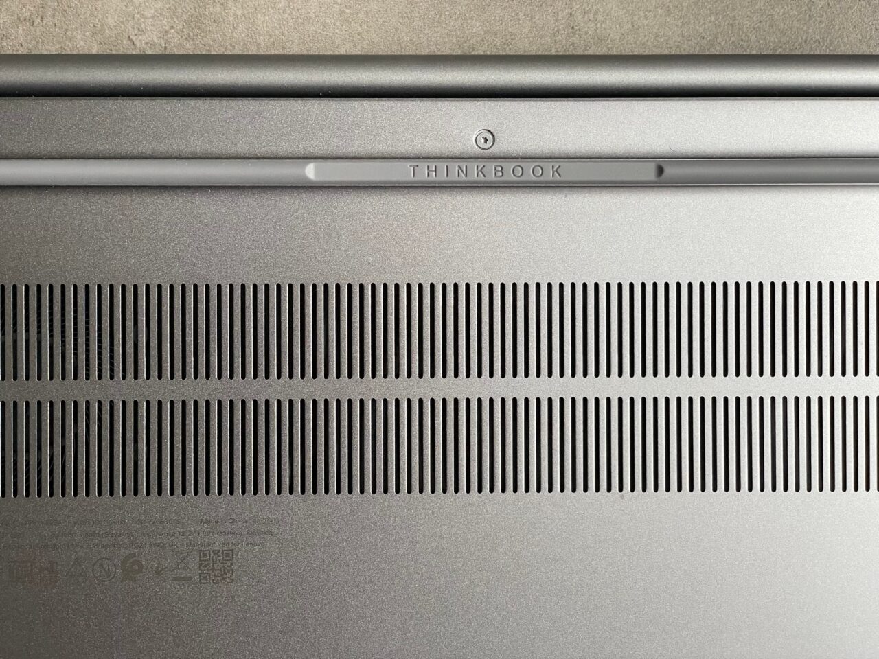 Górna część srebrnego laptopa ThinkBook z charakterystycznym napisem i szczelinami wentylacyjnymi.