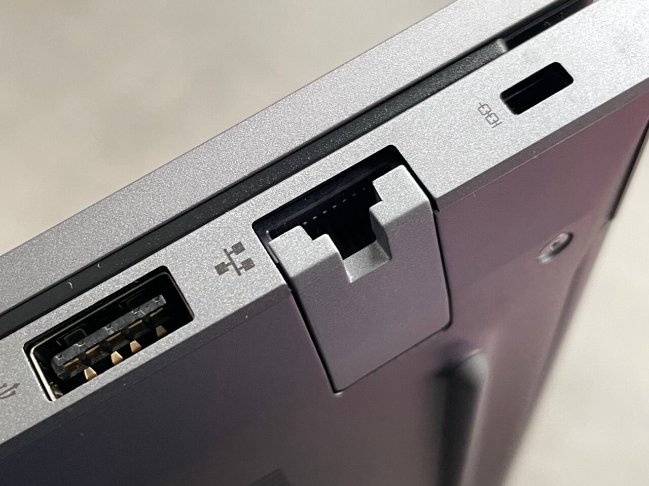 Zbliżenie na porty laptopa, w tym jeden port USB typu A i port Ethernet z wypiętą plastikową osłoną.