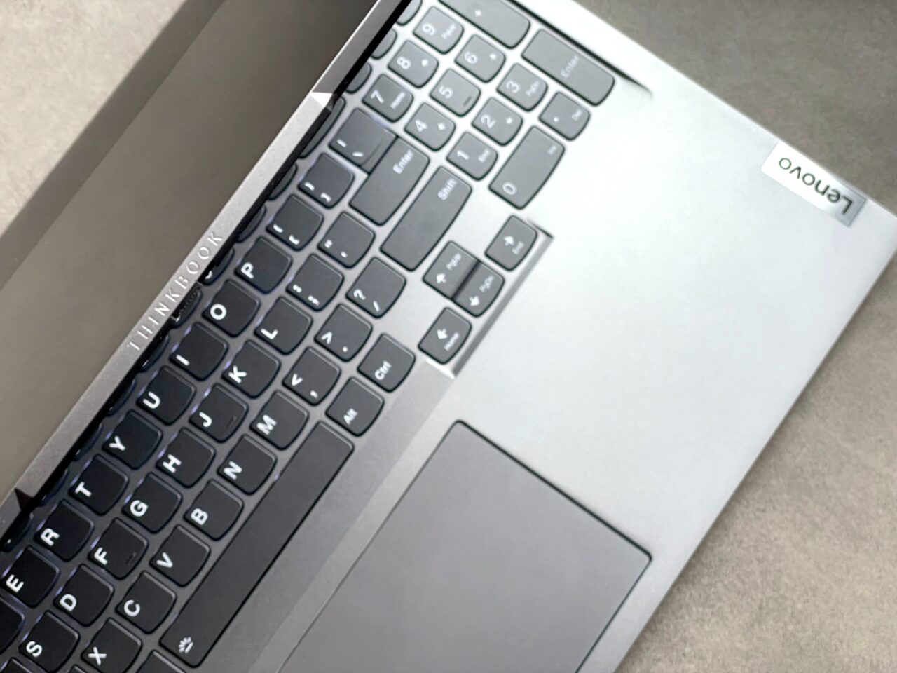Częściowe zbliżenie na klawiaturę laptopa Lenovo ThinkBook z widoczną lewą częścią touchpada i fragmentem czarnej dolnej obudowy.