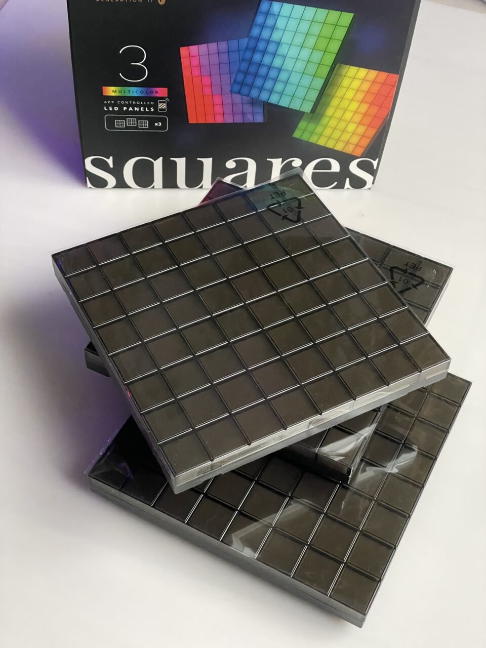 Czarne, kwadratowe panele LED ułożone jeden na drugim na tle opakowania. recenzja Twinkly squares