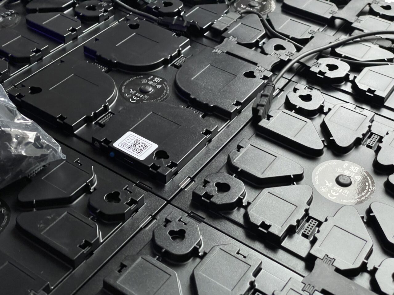 Zdjęcie rozmieszczonych w nieładzie czarnych plastikowych elementów serwerowych z widocznymi przewodami i etykietami QR.