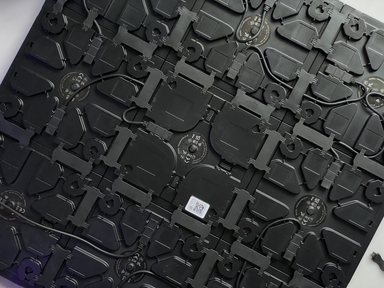 Części z czarnego plastiku różnych kształtów i rozmiarów, prawdopodobnie elektroniczne lub mechaniczne elementy, ułożone chaotycznie jeden na drugim.