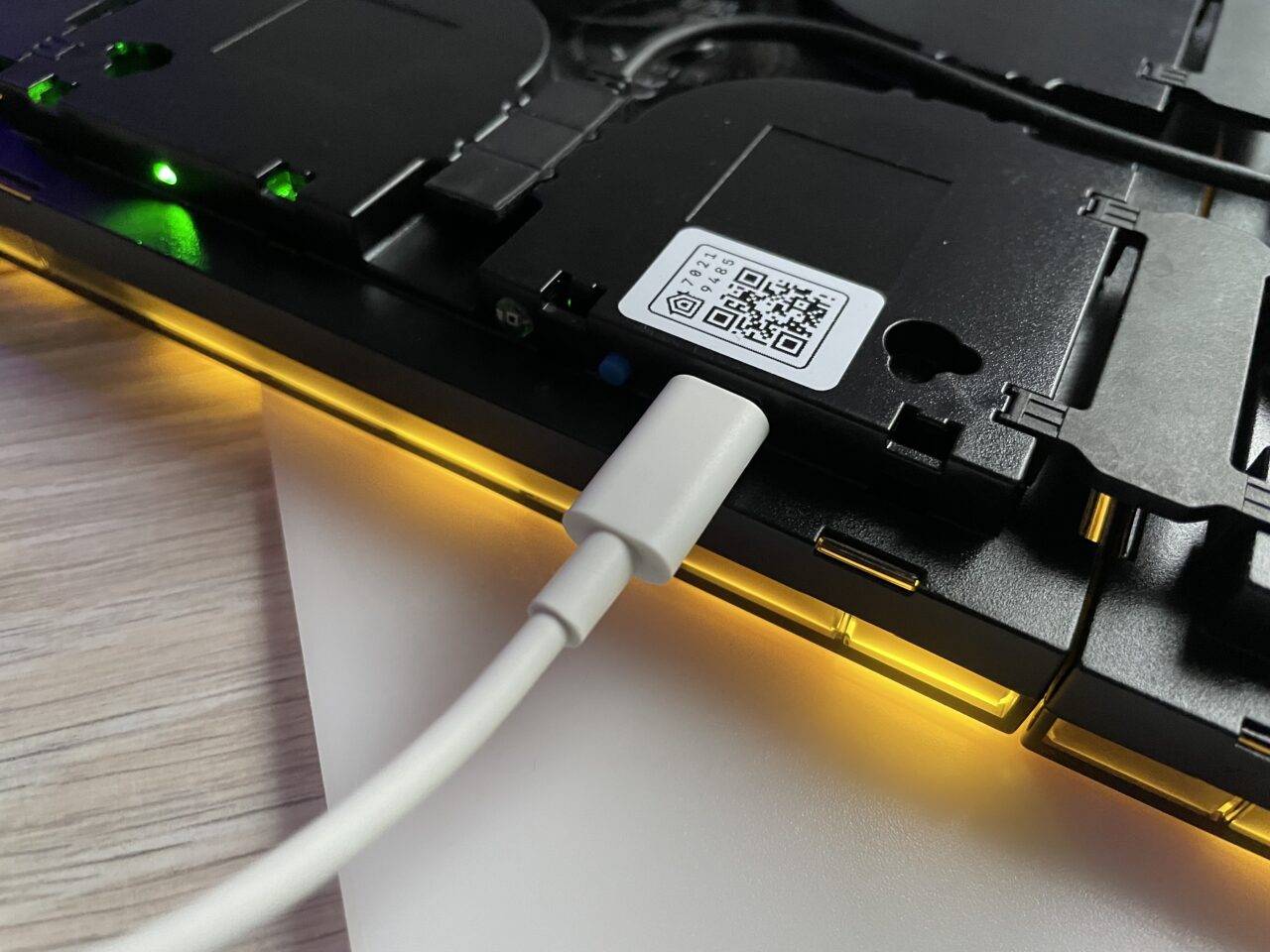 Podłączony biały kabel USB do otwartego laptopa z widocznym kodem QR i podświetleniem RGB na krawędziach.