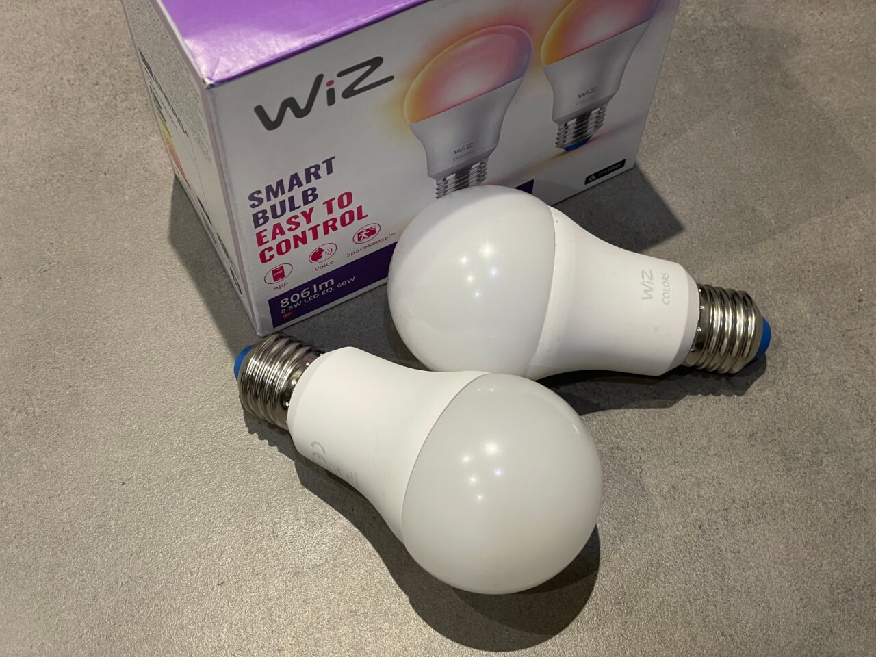 Dwie inteligentne żarówki LED marki WiZ leżące na blacie obok opakowania produktu.