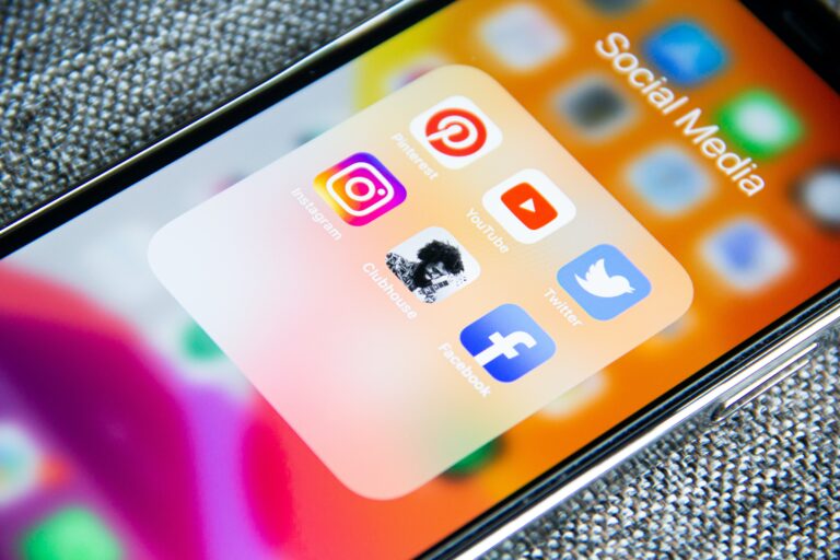 Smartfon z wyświetlonym folderem "Social Media", zawierającym ikony popularnych aplikacji takich jak Instagram, Pinterest, YouTube, Clubhouse, Twitter i Facebook.