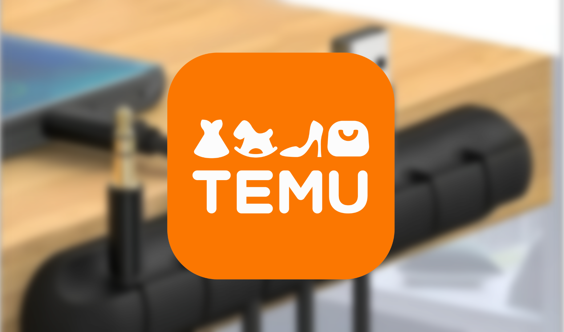 Logo aplikacji Temu z ikonami ubrań i akcesoriów na pomarańczowym tle, rozmyte biurko w tle.