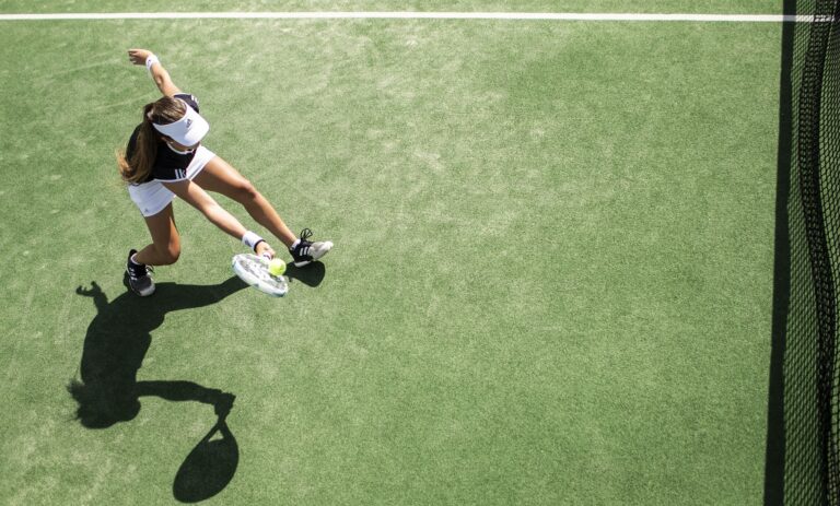 Kobieta w sportowym stroju grająca w tenisa na zielonym korcie, wykonująca zamaszysty ruch rakietą do odbicia piłki.