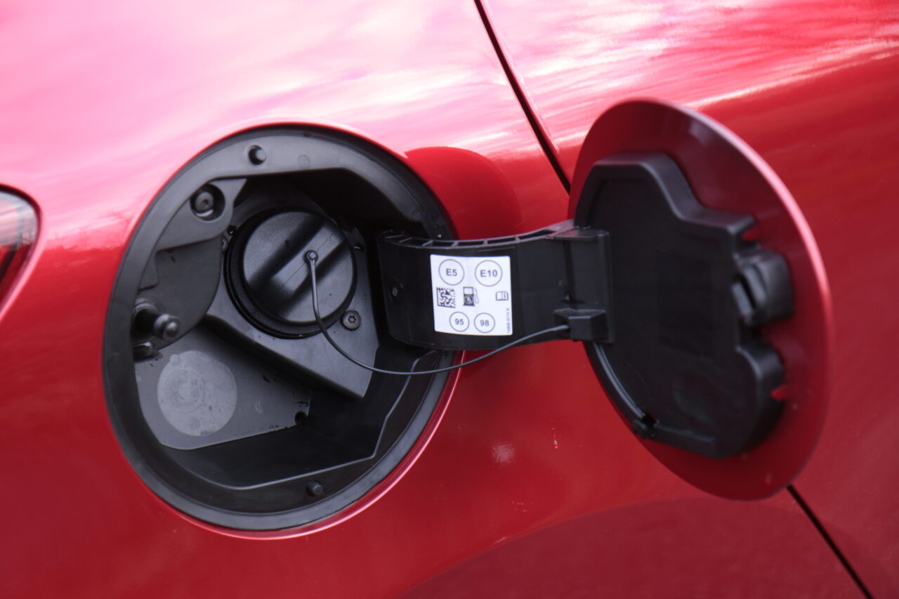 Klapka wlewu paliwa w czerwonym Mitsubishi Colt z otwartą klapką i widocznym naklejką informacyjną o odpowiednich typach paliwa. Zasięg i spalanie
