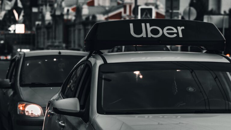 Samochód z charakterystycznym logo "Uber" na dachu, na tle miejskiej ulicy.