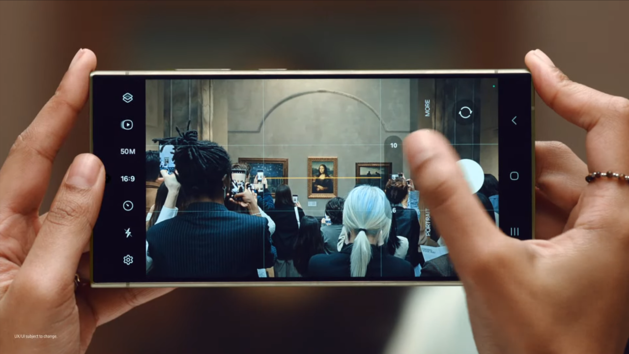 Osoba trzymająca smartfon i fotografująca przez ekran tłum ludzi robiących zdjęcia obrazowi Mona Lizy w muzeum.