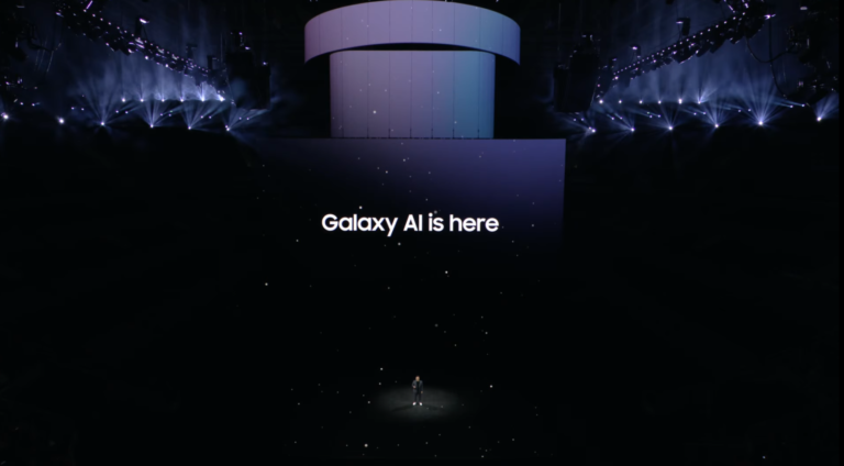 Duża scena podświetlona na ciemno z osobą stojącą na środku i napisem "Galaxy AI is here" wyświetlanym nad sceną.