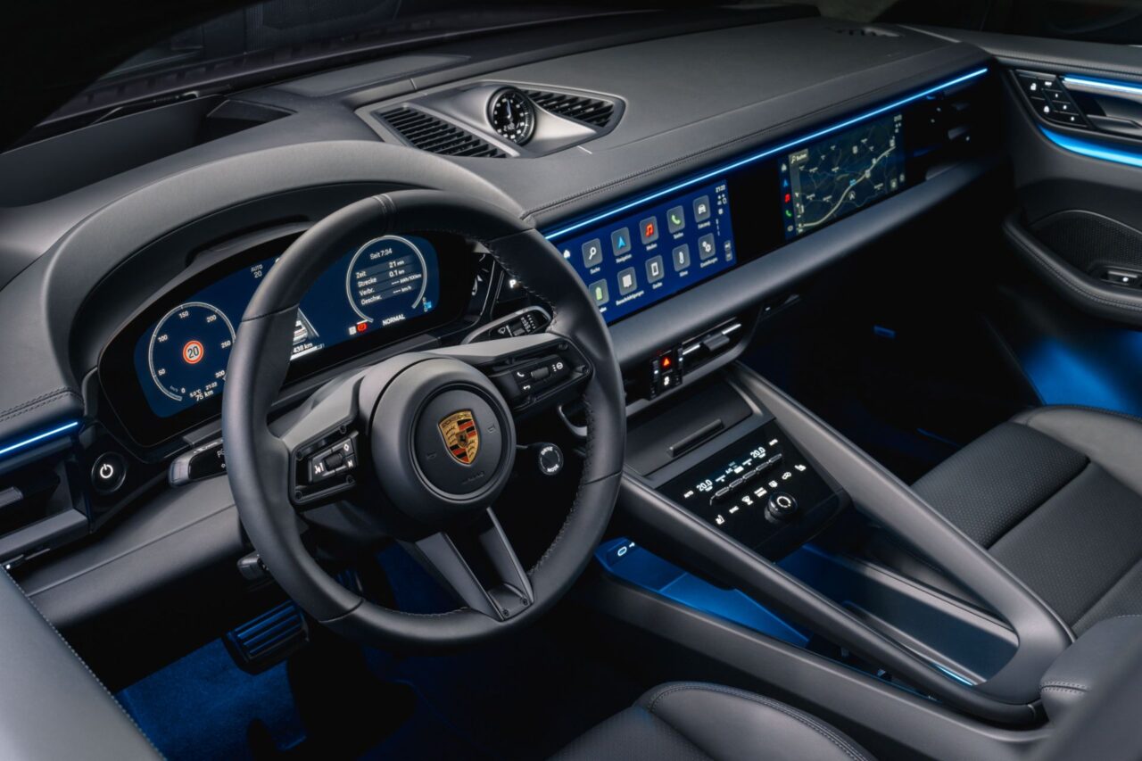 Wnętrze samochodu Porsche z widokiem na kierownicę, deski rozdzielczej z cyfrowymi wskaźnikami i duży ekran dotykowy systemu multimedialnego.