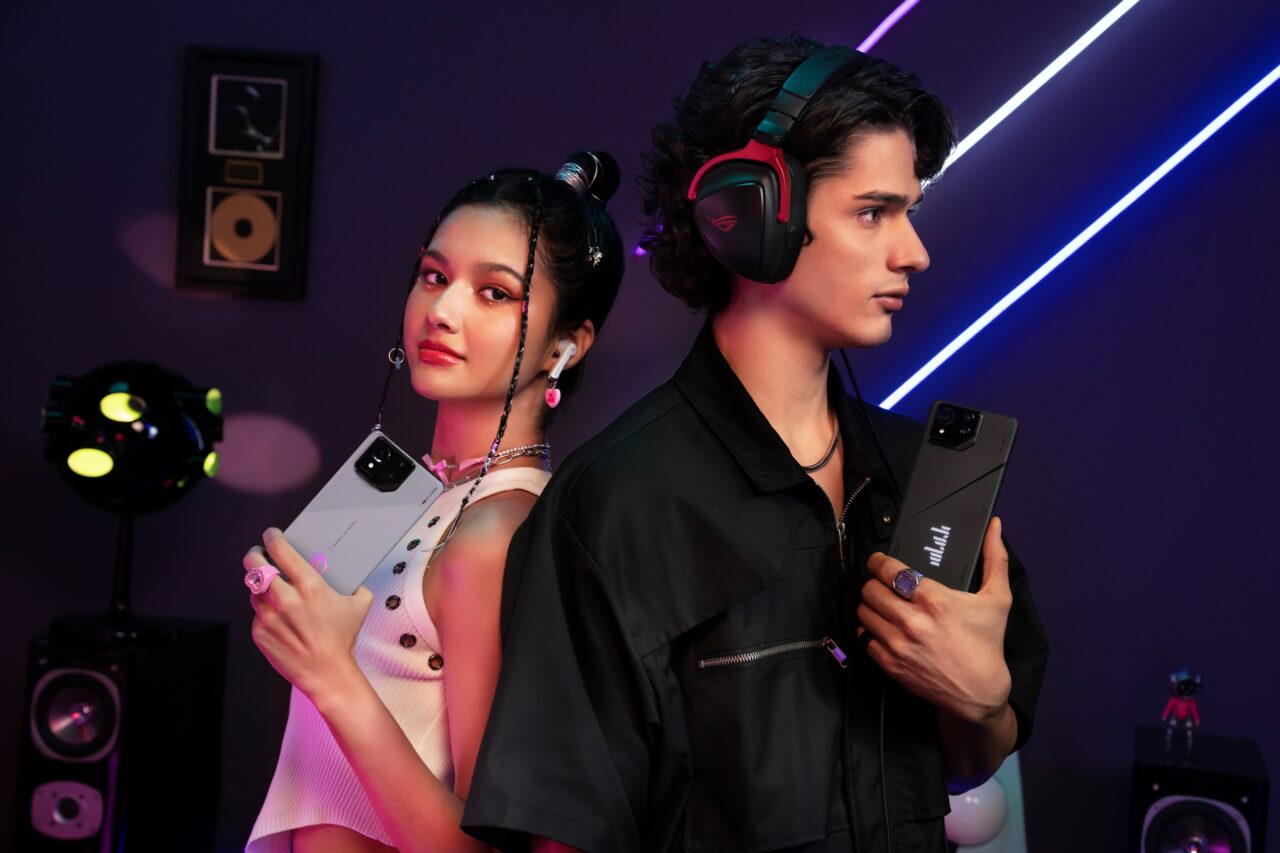 Dwoje młodych ludzi pozuje z akcesoriami do słuchania muzyki i smartfonami na tle fioletowo-niebieskiego oświetlenia. Kobieta trzyma smartfona i nosi słuchawki douszne, a mężczyzna ma na głowie duże słuchawki i trzyma w dłoni smartfona.