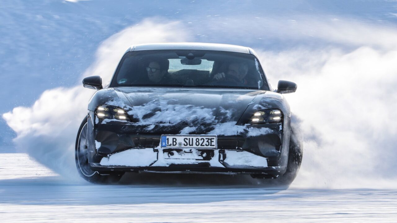 Porsche Taycan. Czarny samochód elektryk jedzie z dużą prędkością po zasypanej śniegiem drodze, wokół unosi się chmura śniegu.