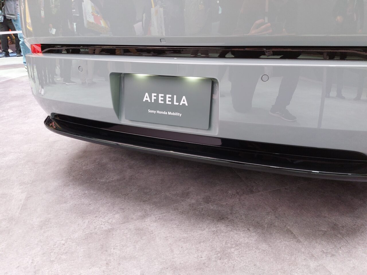 Tylna część szarego samochodu z wyświetlaczem LED na tablicy rejestracyjnej, na którym widnieje napis "AFEELA - Sony Honda Mobility".