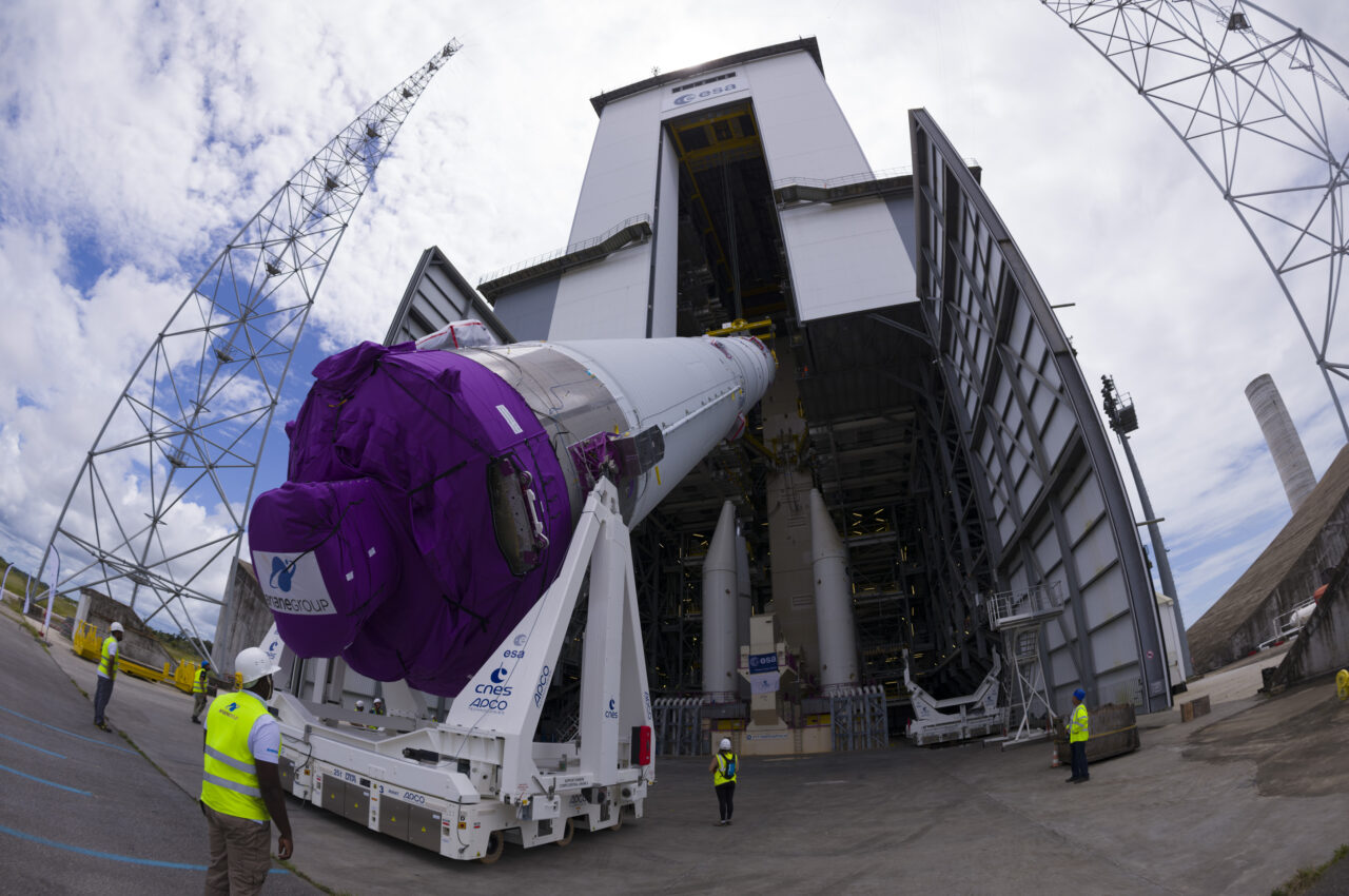 Rakieta kosmiczna Ariane 6 transportowana przed startem, osłonięta fioletową osłoną, z pracownikami w kamizelkach odblaskowych i hangarem w tle. przyszłe misje kosmiczne ESA zależą od niej