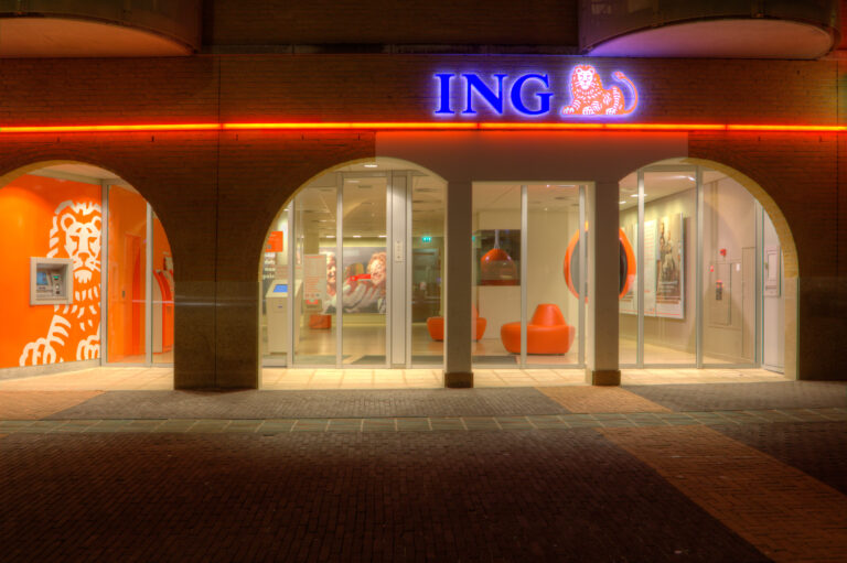 Oddział banku ING w nocy, z pomarańczowym wnętrzem i firmowym logo nad wejściem.