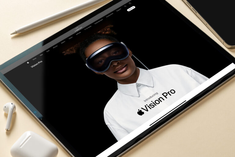 Tablet prezentujący stronę internetową z obrazem kobiety w białej koszuli z logo "Vision Pro" i noszącej futurystyczne okulary Apple Vision Pro. Obok tabletu leżą bezprzewodowe słuchawki i etui do nich.