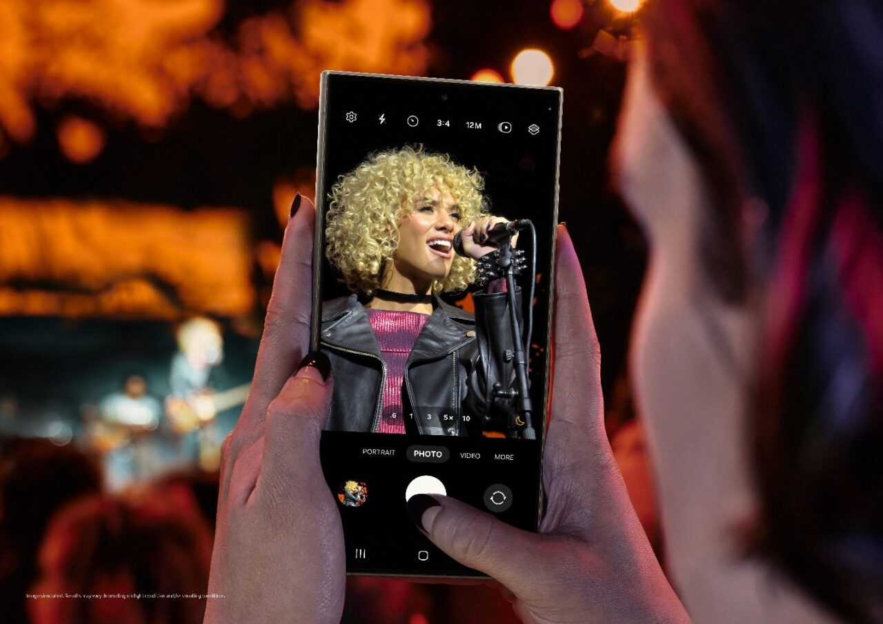 Osoba robi zdjęcie smartfonem Samsung Galaxy S24 Ultra, na ekranie piosenkarka, widz jest częściowo widoczny w tle.
