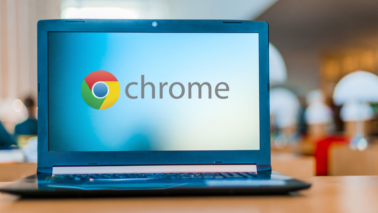 Laptop na mesa com o logotipo do Google Chrome exibido na tela, fundo desfocado do interior do escritório.