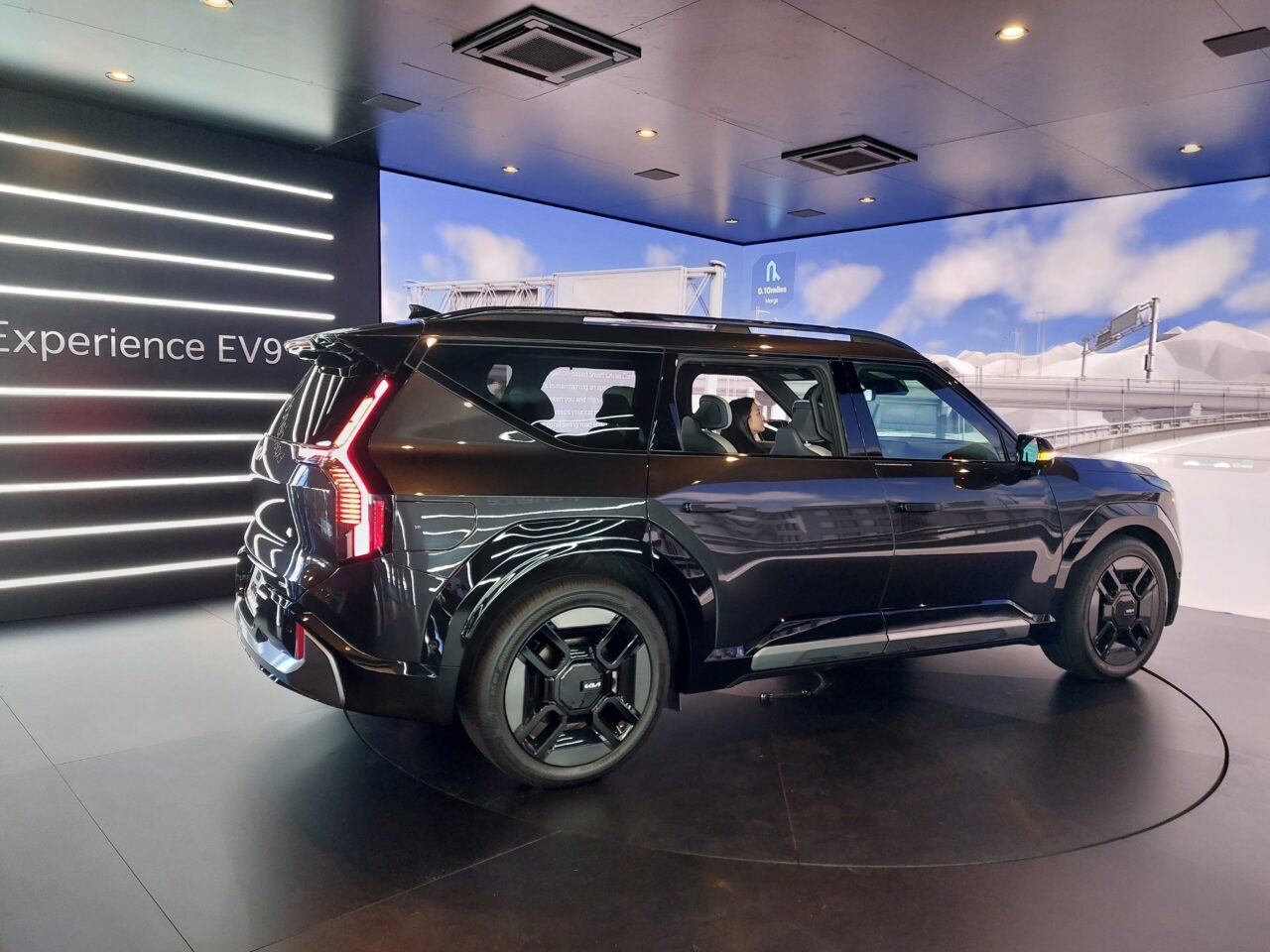 Czarny SUV wystawiony w salonie z oświetleniem LED i napisem „Experience EV9” w tle.