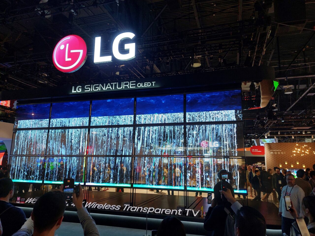 Ekspozycja telewizorów LG Signature OLED T na targach CES 2024, z dużym logo LG i wizualizacją wodospadu na ekranach, w tle widoczni odwiedzający robiący zdjęcia.