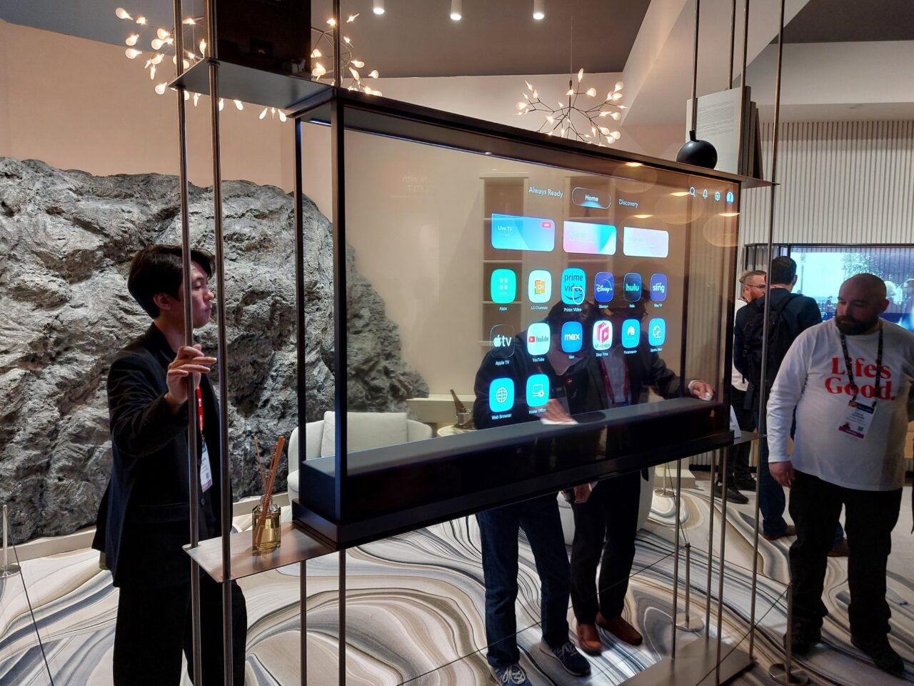 Osoby oglądające przeźroczysty ekran LG Signature OLED T wyświetlający interfejs smart TV w nowoczesnym wnętrzu. Stoisko LG na targach CES 2024