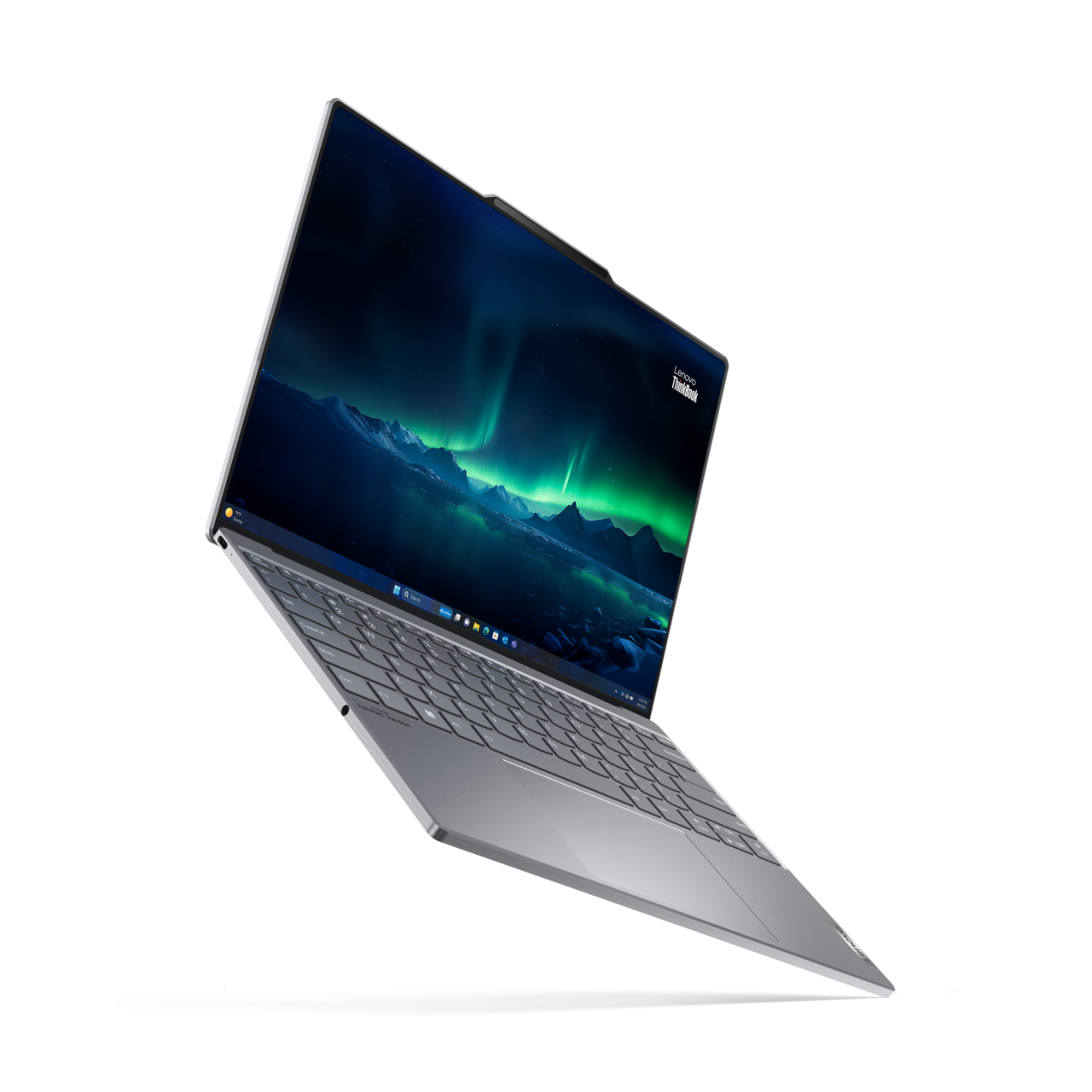 Laptop Lenovo ThinkBook na białym tle z włączonym ekranem przedstawiającym górski krajobraz i zorzę polarną, z klawiaturą o szarym wykończeniu.