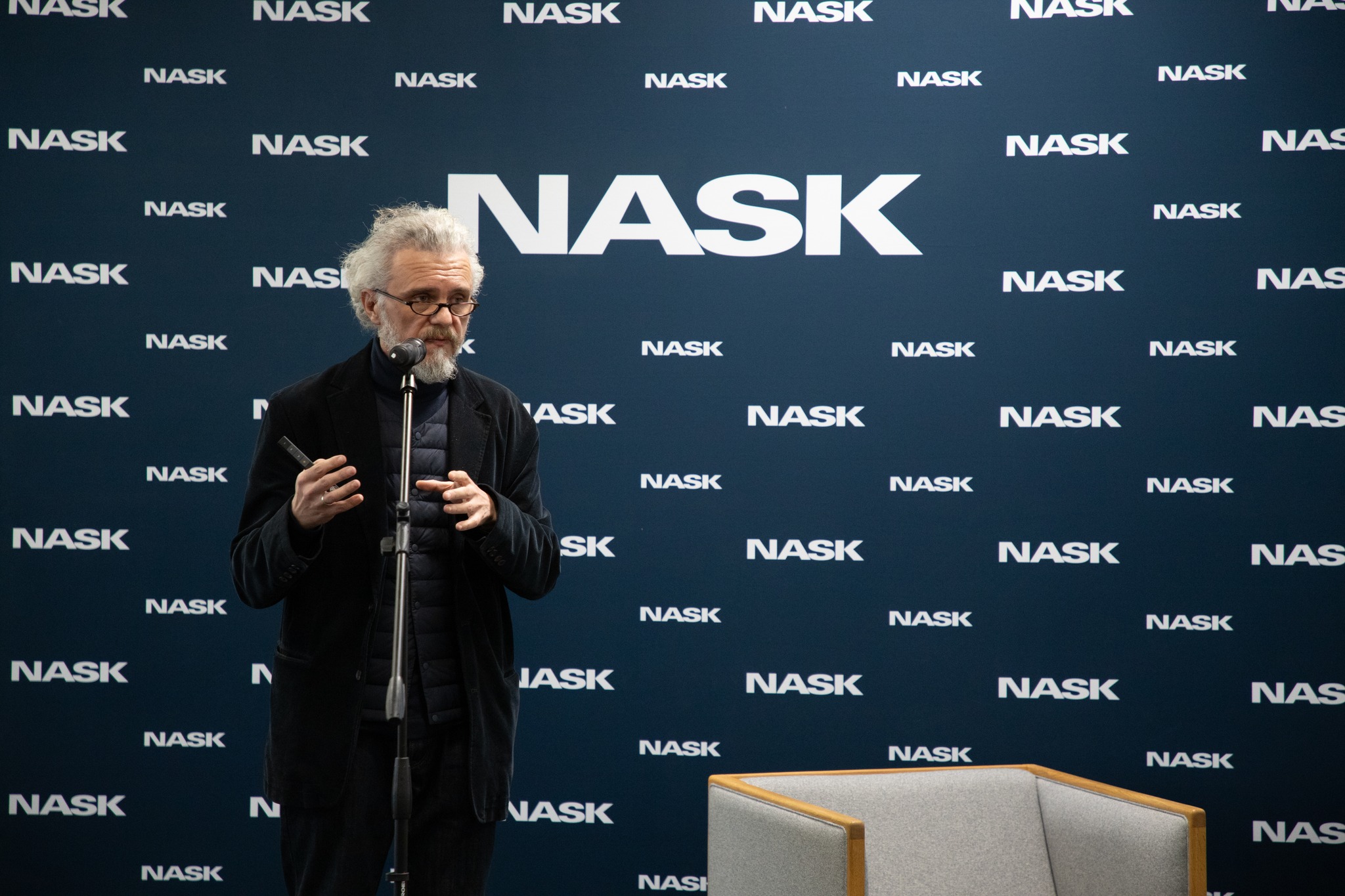 Starszy mężczyzna przemawia do mikrofonu przed tłem z logo NASK.