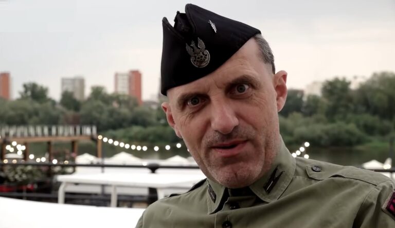 Wojciech Olszański - Mężczyzna w wojskowym mundurze i berecie stojący na tle rzeki i drzew.