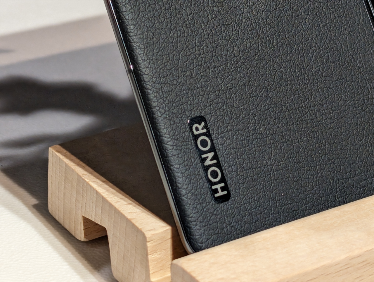 Czarny skórzany etui na smartfon z wygrawerowanym logo "HONOR", oparty na drewnianym stojaku.