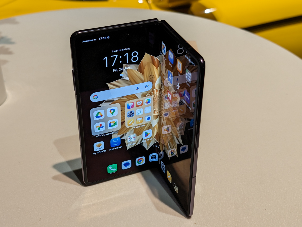 Złożony smartfon na białym stole pokazujący kolorowy ekran główny z ikonami aplikacji.
