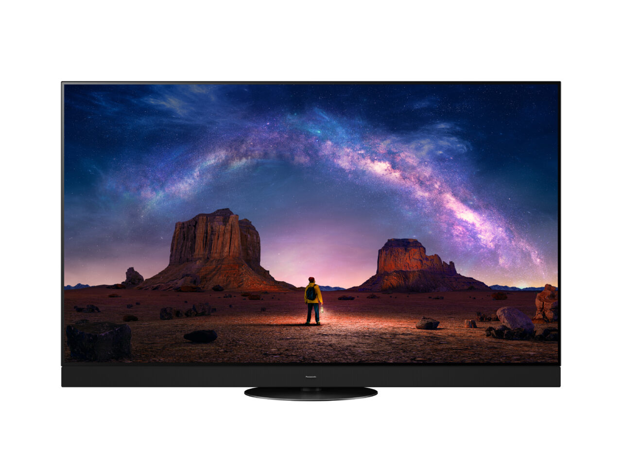 Telewizor wyświetlający obraz pustyni z formacjami skalnymi w nocy pod rozgwieżdżonym niebem z widoczną Drogą Mleczną oraz sylwetką człowieka.