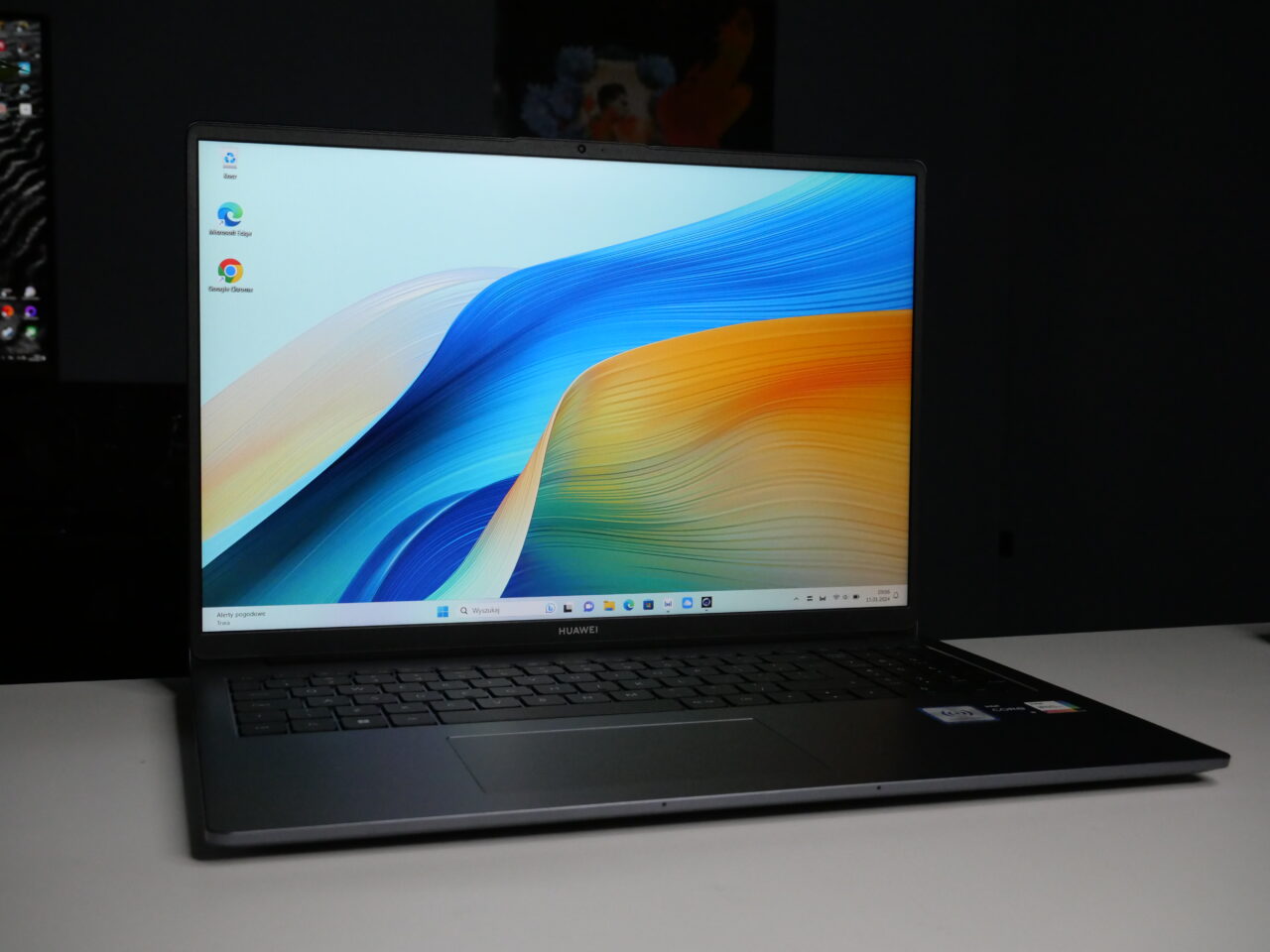 Laptop Huawei z otwartą pokrywą i wyświetlonym pulpitem na ciemnym biurku.