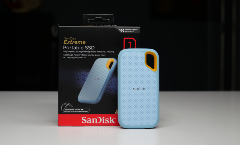 Zdjęcie przenośnego dysku SSD marki SanDisk Extreme w niebieskim etui, stojącego obok oryginalnego pudełka produktu, na białej powierzchni z czarnym tłem.