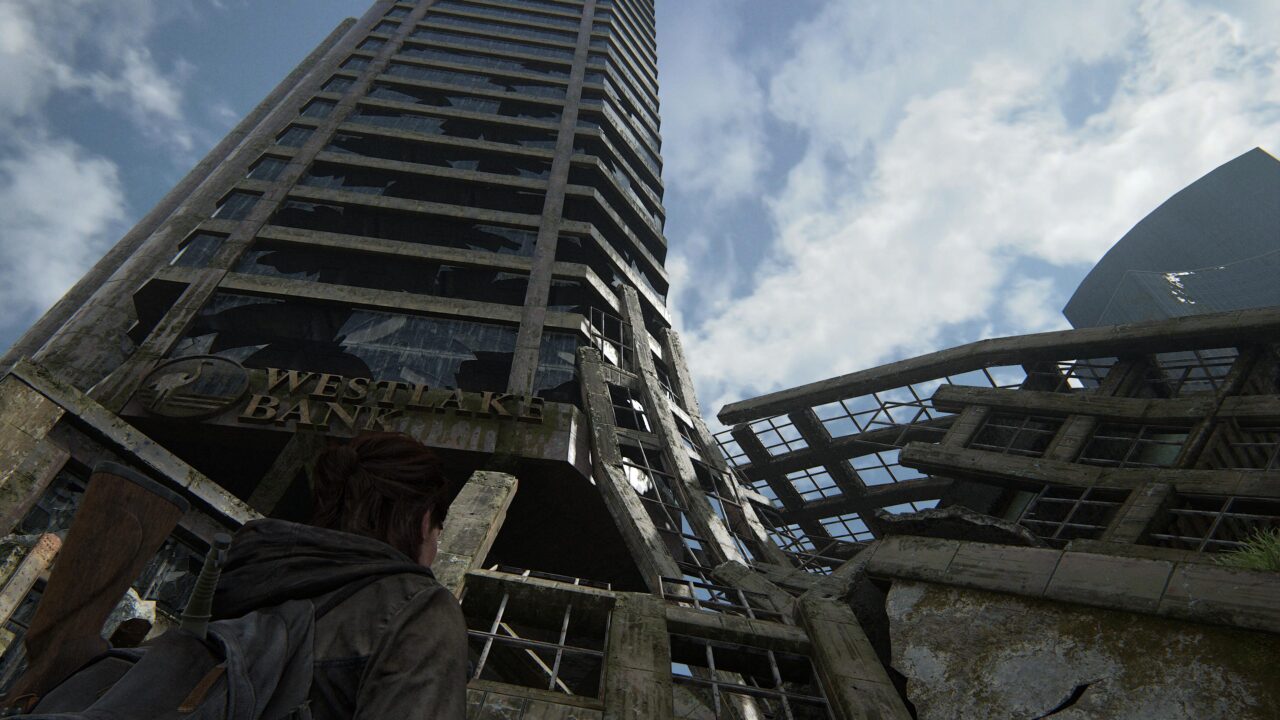 Zrujnowane, opuszczone wieżowce zniszczone przez katastrofę, z pierwszoplanową postacią obserwującą scenerię. Screen z gry The Last of Us Part II Remastered.