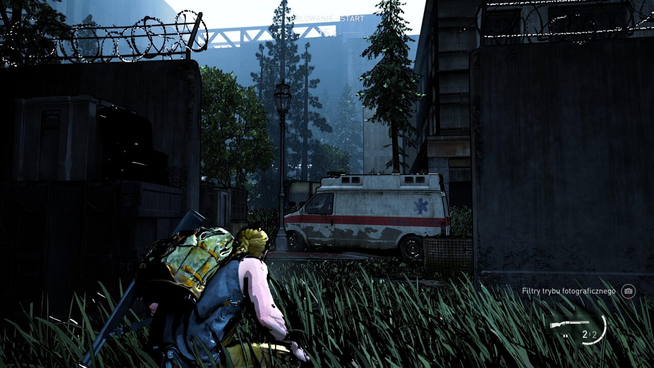 Postać w grze wideo skrada się obok zardzewiałej karetki pogotowia w opuszczonym, miejskim otoczeniu z widocznym drutem kolczastym i zaroślami.