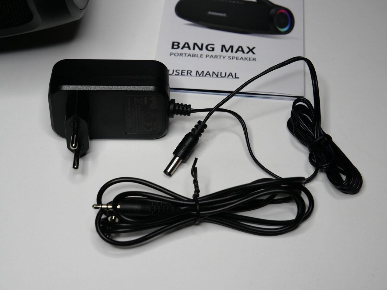 Czarny zasilacz sieciowy oraz przewód ze złączem typu jack na białym tle obok instrukcji obsługi głośnika przenośnego BANG MAX.