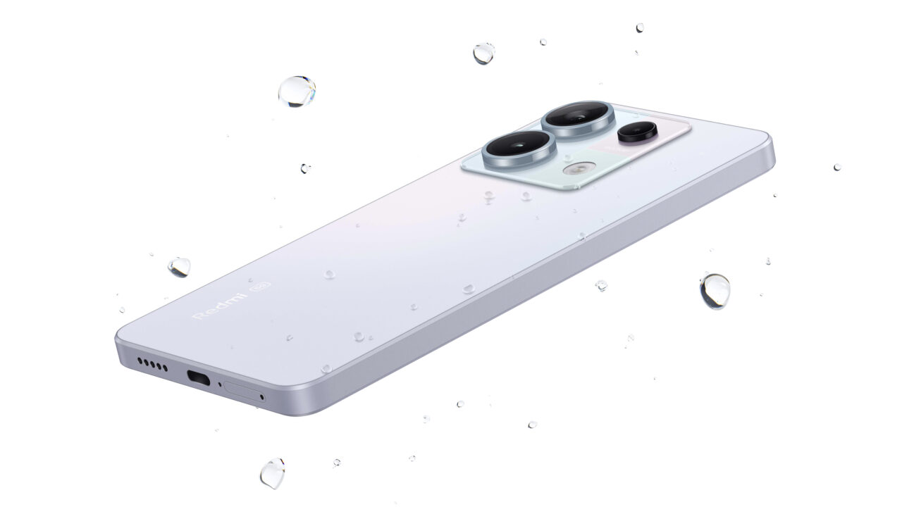 Biały smartfon Redmi Note 13 5G leżący przekręcony na bok z kroplami wody na powierzchni, z trzema obiektywami aparatu i logo Redmi widocznym.