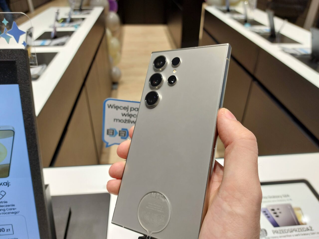 Osoba trzyma srebrny smartfon z pięcioma obiektywami kamery z tyłu w sklepie elektronicznym.