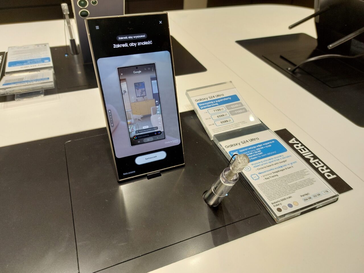 Smartfon Galaxy S24 Ultra wyświetlający aplikację z artykułami domowymi, umieszczony na wystawie sklepowej z informacją o produkcie i ceną.