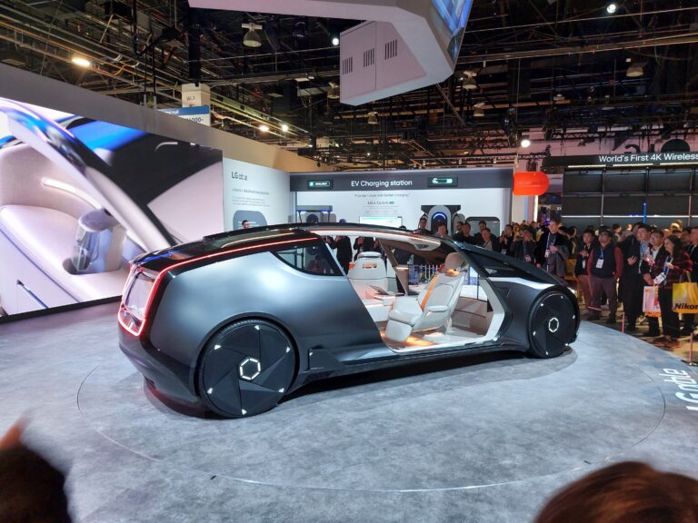 Koncept luksusowego samochodu elektrycznego prezentowany na targach, z otwartymi drzwiami i widokiem na futurystyczne wnętrze, otoczony przez grupę oglądających osób.