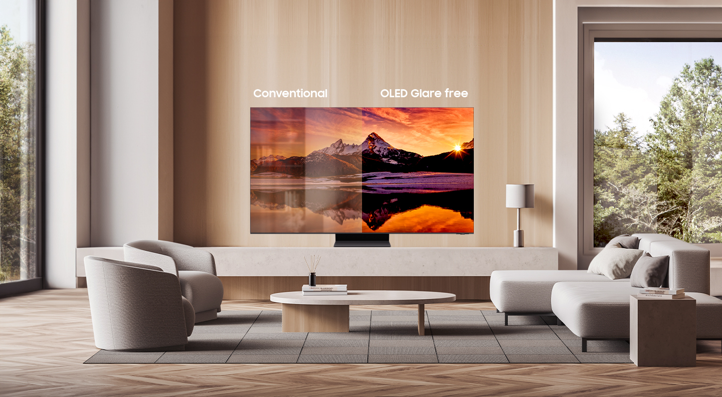 Nowoczesny salon z dużym telewizorem OLED pokazującym zdjęcie krajobrazu, z napisami "Conventional" i "OLED Glare free" wskazującymi na porównanie jakości obrazu, otoczony przez dwa stylowe fotele i sofę, z dużymi oknami w tle z widokiem na drzewa.