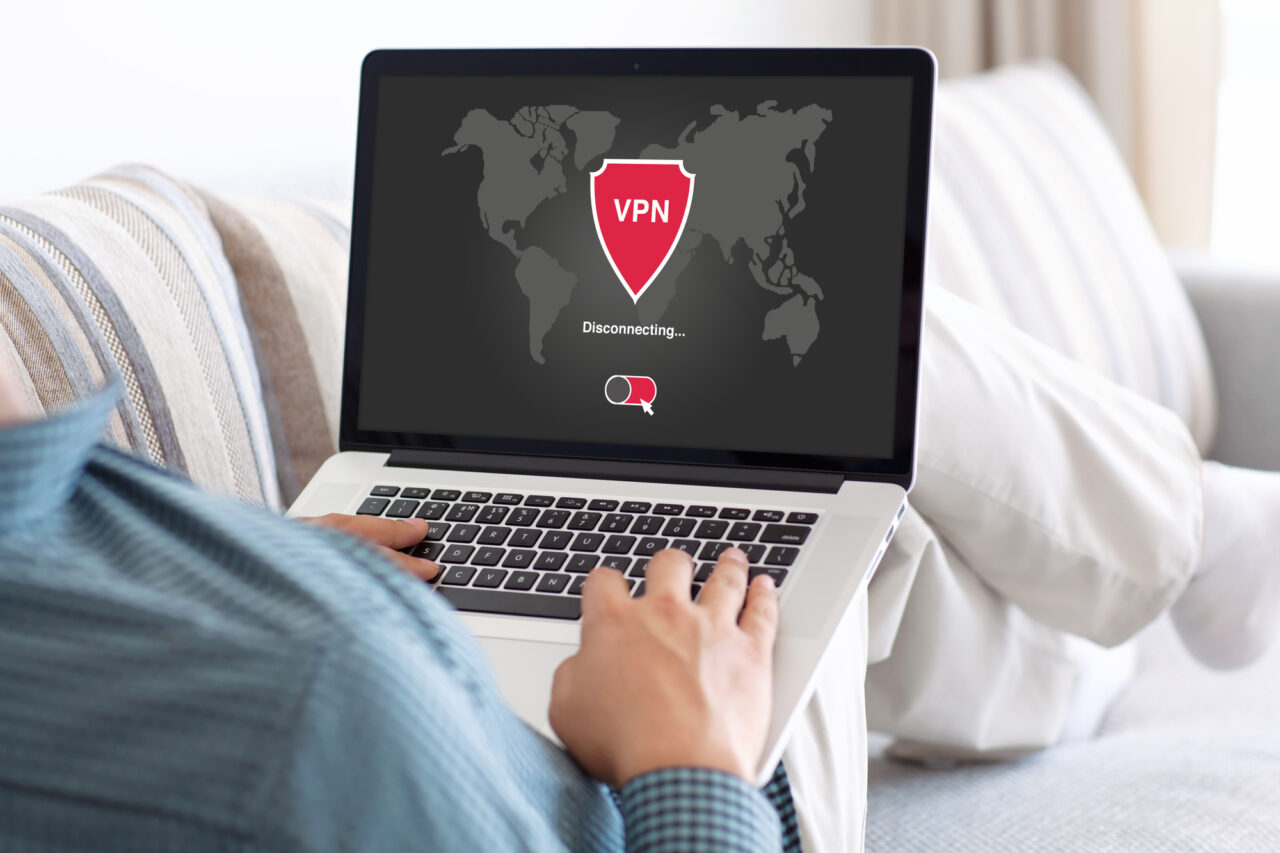 Osoba używająca laptopa z ekranem wyświetlającym mapę świata i ikoną VPN oraz napisem "Rozłączanie...". Zdjęcie ilustrujące co to VPN.