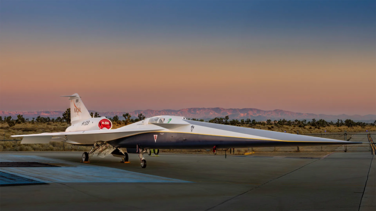 Eksperymentalny samolot odrzutowy NASA X-59 QueSST na lotnisku o zmierzchu, z górami w tle i różowym niebem.