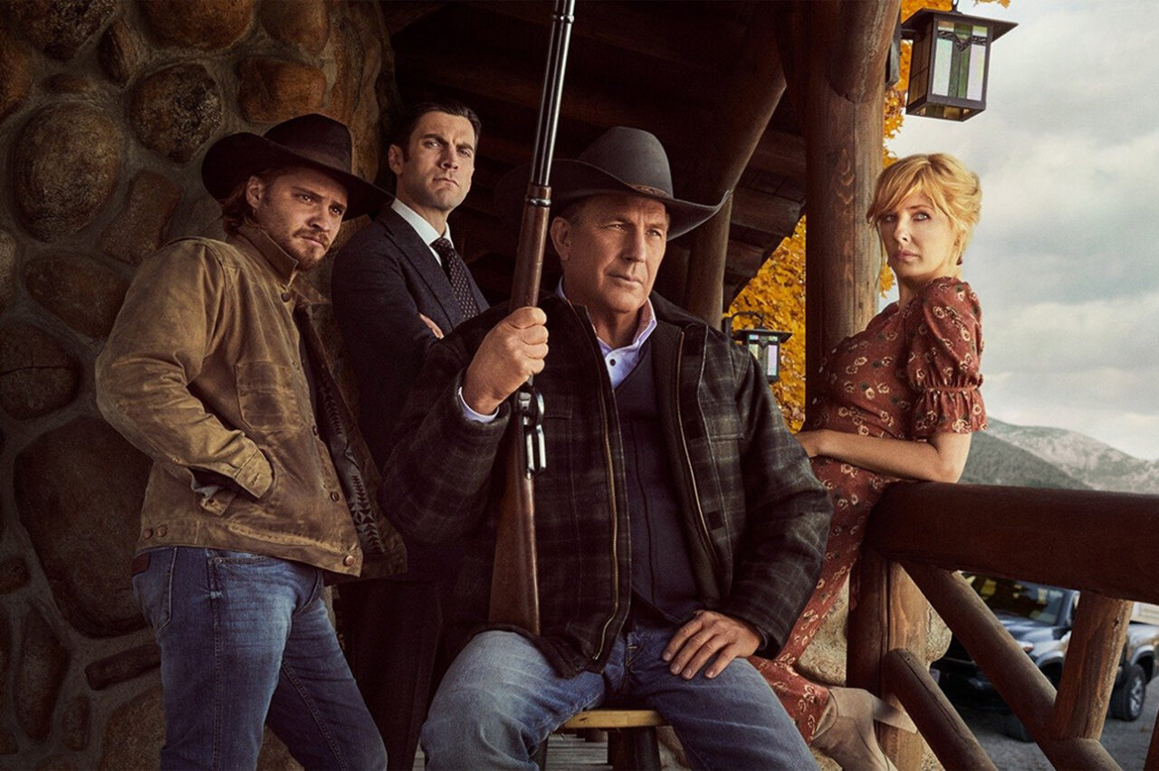 Zdjęcie do artykułu pt. gdzie obejrzeć Yellowstone - czterech dorosłych, trzech mężczyzn i kobieta, ubrani w stylu współczesnym westernowym, stoją na werandzie domu z bali. Mężczyzna na pierwszym planie trzyma strzelbę, a w tle widać góry. Kadr z serialu Yellowstone dostępnego na Netflix.