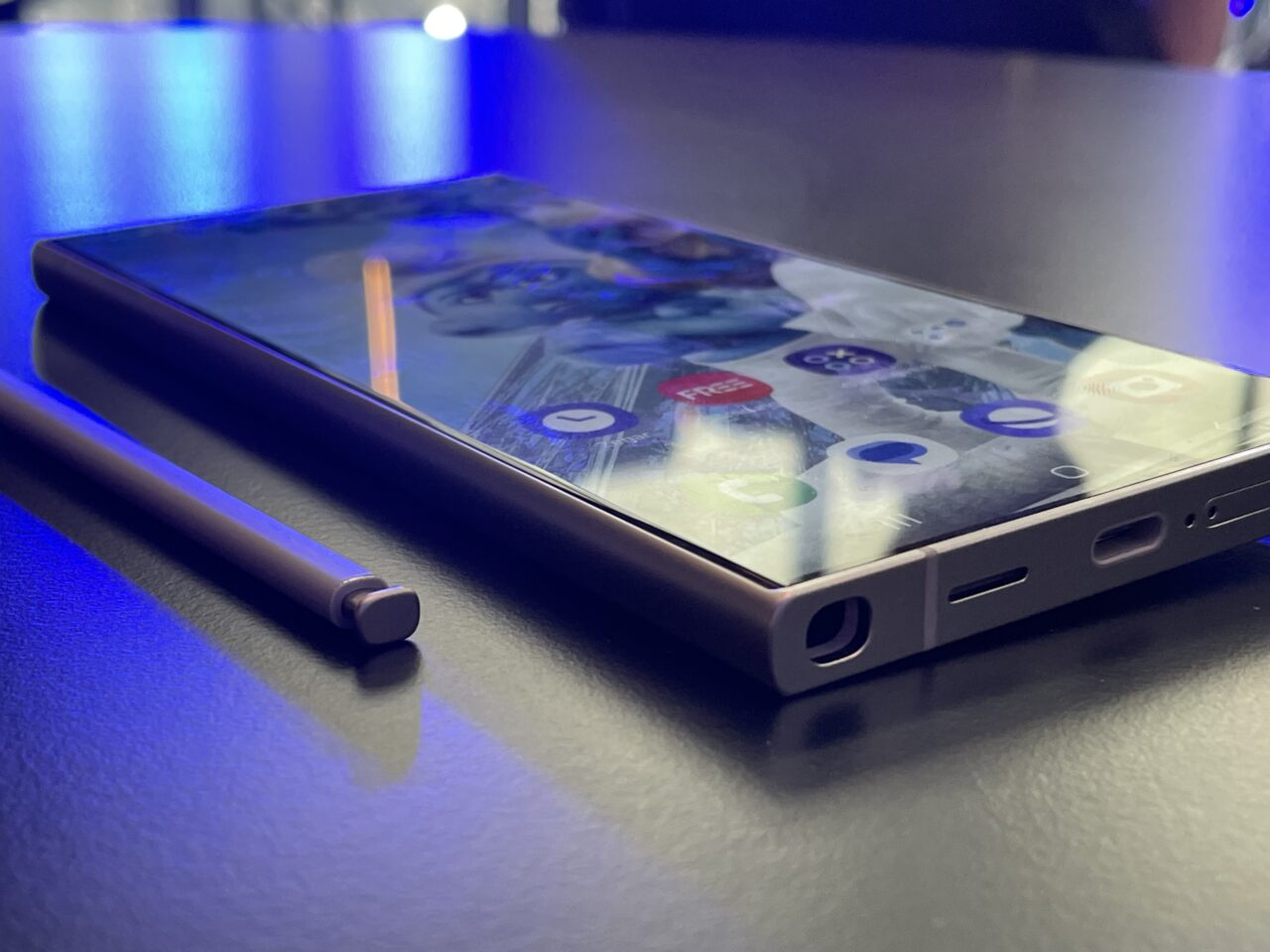 Nowoczesny smartfon Samsung Galaxy S24 Ultra leżący na błękitnej powierzchni obok cyfrowego rysika, z odbiciem świateł w tle.